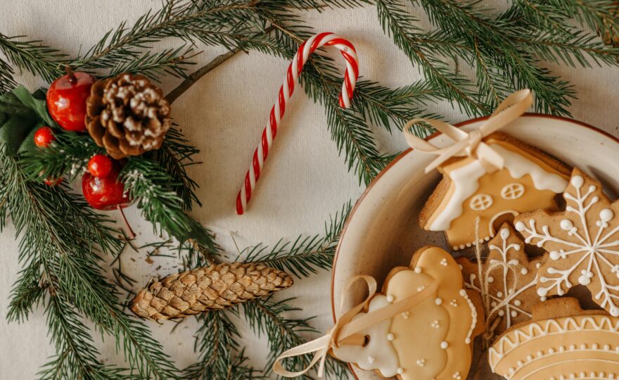 På ett bord ligger granris, en polkagrisstång, kottar och pepparkakor med glasyr.