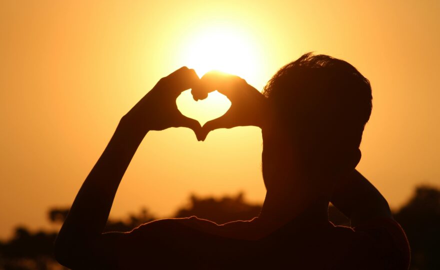 En man formar sina fingrar som ett hjärta och håller upp händerna mot solen.